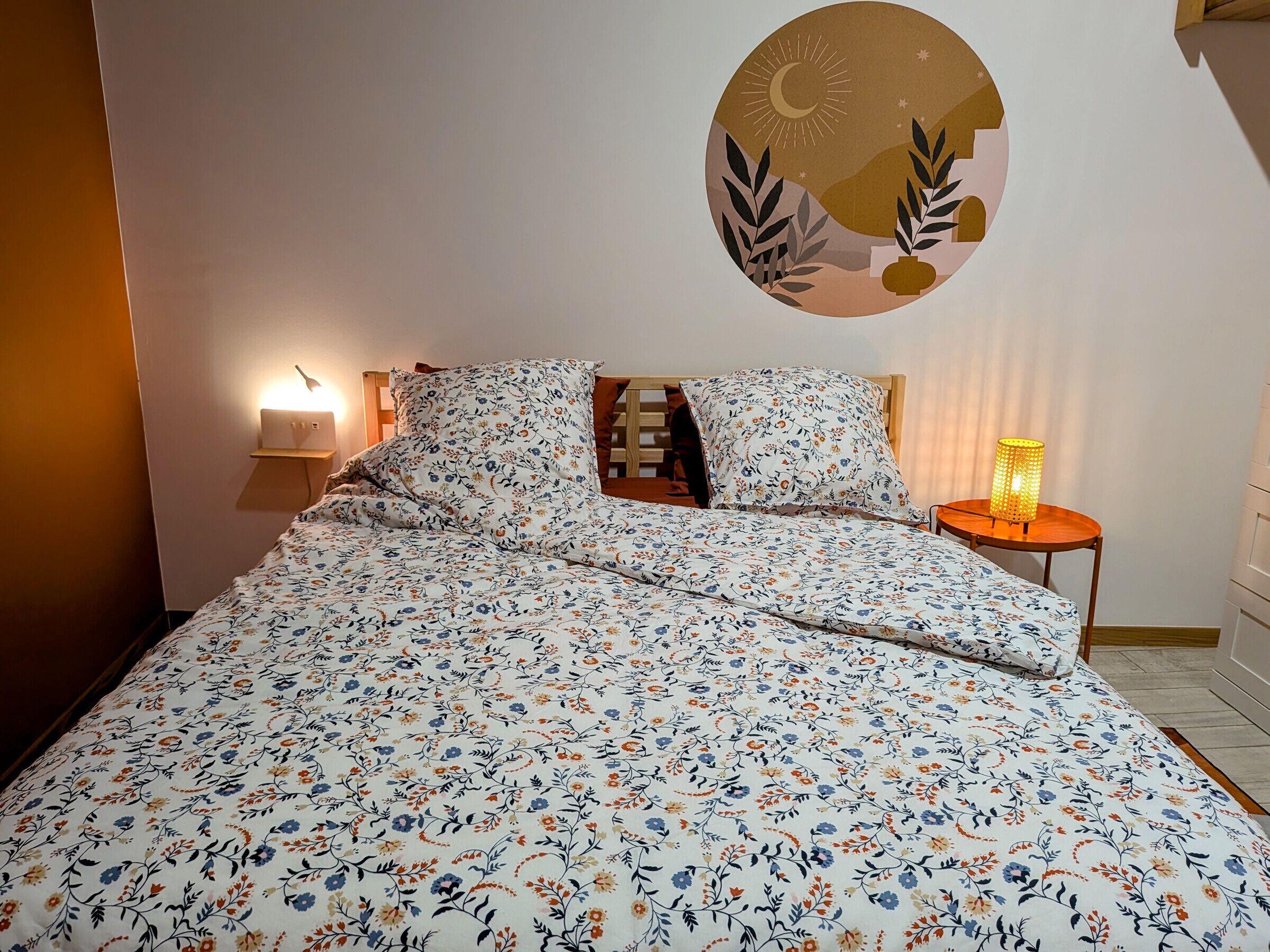 A bed with floral bedding, a bedside lamp, and a wall clock.