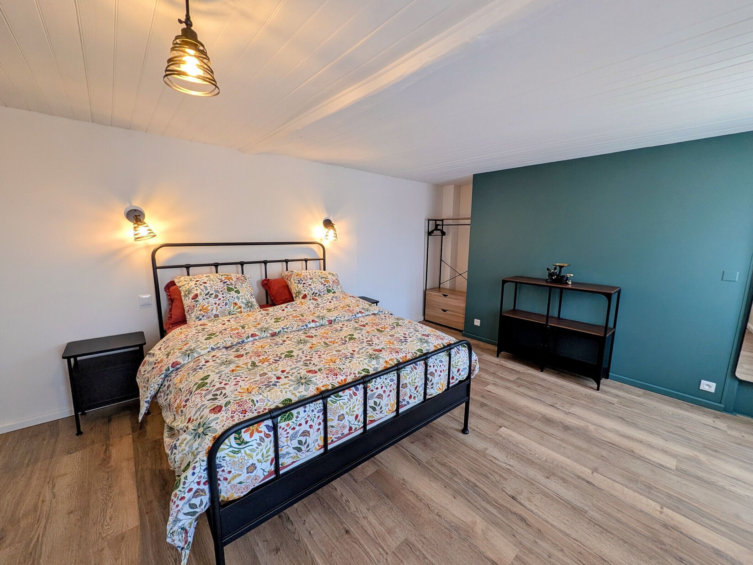 Een slaapkamer met een bed, nachtkastjes, een kledingkast en een bureau met stoel.
