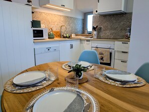 A dining table set with plates, glasses, and cutlery, a microwave, and a coffee machine in a kitchen with white cabinets and a patterned backsplash.