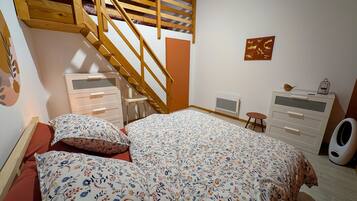 Un dormitorio con escaleras de madera, una cama con ropa de cama floral, un aparador, un radiador y un taburete pequeño.