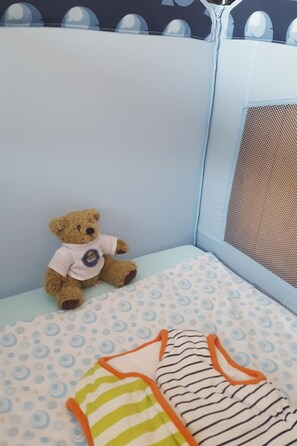 Ein Spielbereich für Kinder mit einem Teddybär, einem Bett mit gemustertem Bettbezug und einem Insektenschutznetz.