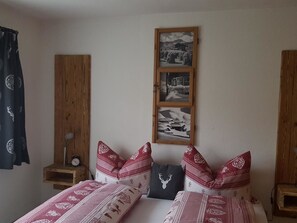 A bedroom with two beds, patterned bedding, a wall-mounted picture frame with multiple images, and a small bedside table with a lamp. - Chalet Waldperle Appartement/Fewo, Dusche, WC, 2-Bettwohnung by Interhome (Arosa)