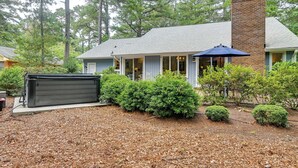 A house with a brick chimney, a covered porch, and a small garden with mulch and shrubs. - Walk to Golf! Relax With Hot Tub and Game Room! (Pinehurst)