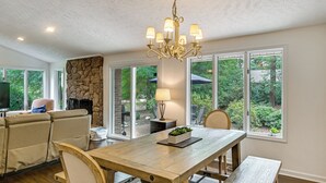A dining area with a wooden table, chairs, a chandelier, and a stone fireplace. - Walk to Golf! Relax With Hot Tub and Game Room! (Pinehurst)