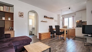 Un salon moderne comprenant un canapé, un coin repas avec des chaises, un téléviseur et un espace cuisine avec des placards.