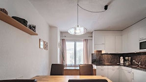 Une cuisine moderne avec un coin repas, comprenant une table et des chaises en bois, un luminaire suspendu et une vue par la fenêtre.