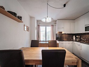 Eine moderne Küche mit Essbereich, mit einem Holztisch und Stühlen, einer Hängeleuchte und Blick durch das Fenster.