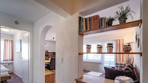 Un intérieur moderne avec un meuble en bois, une étagère avec des livres et des plantes, et une vue sur un espace cuisine.