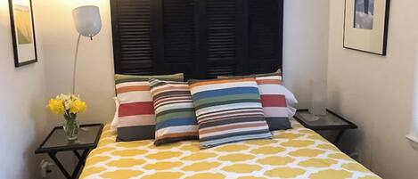 A neatly made bed with a yellow and white patterned bedspread, flanked by two bedside tables with lamps and a vase of flowers.