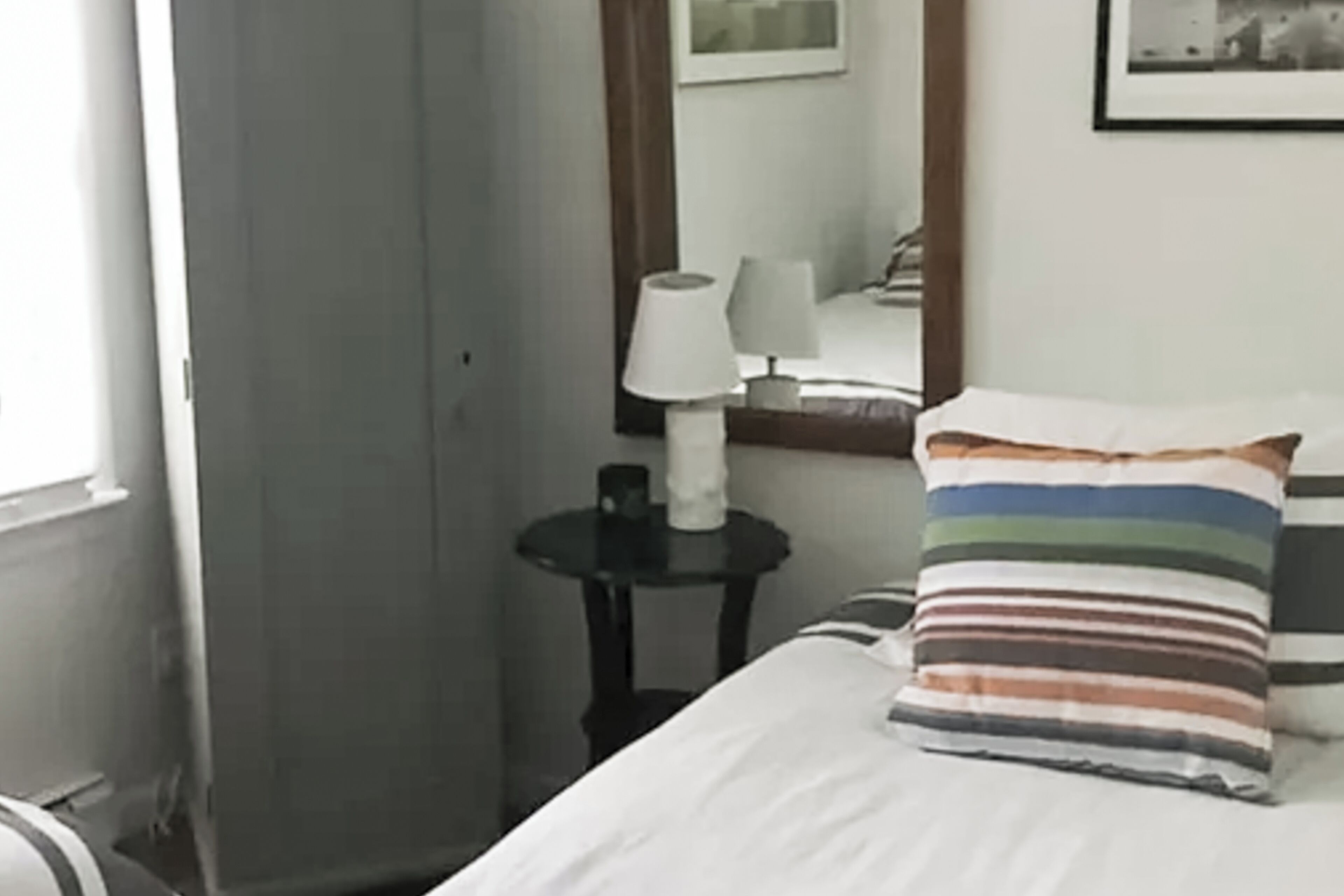 Ein Hotelzimmer mit einem Bett, einem Nachttisch mit Lampe, einem gestreiften Kissen und einem Spiegel an der Wand.