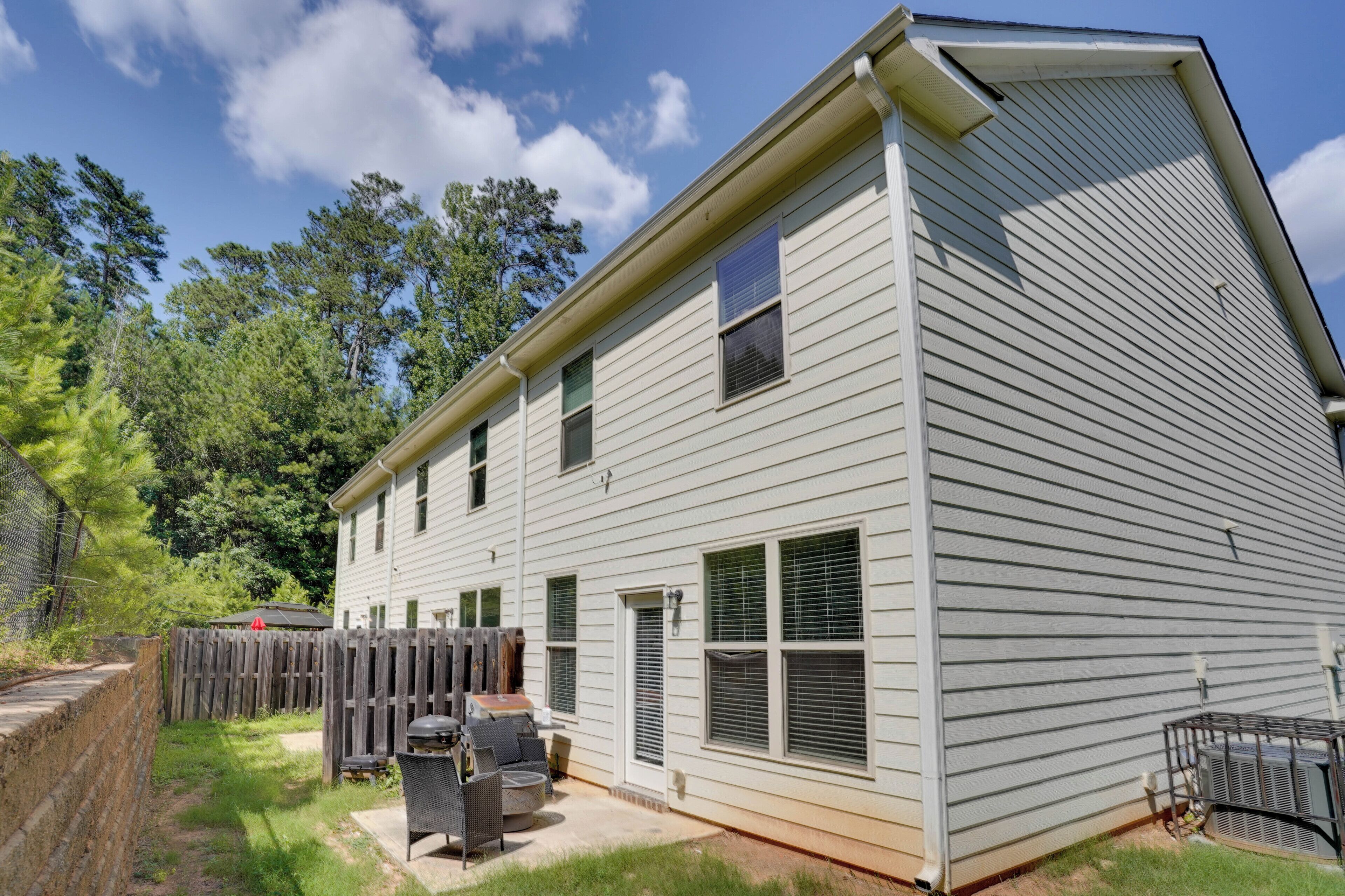 A two-story house with a fenced backyard, outdoor seating, and a visible air conditioning unit.