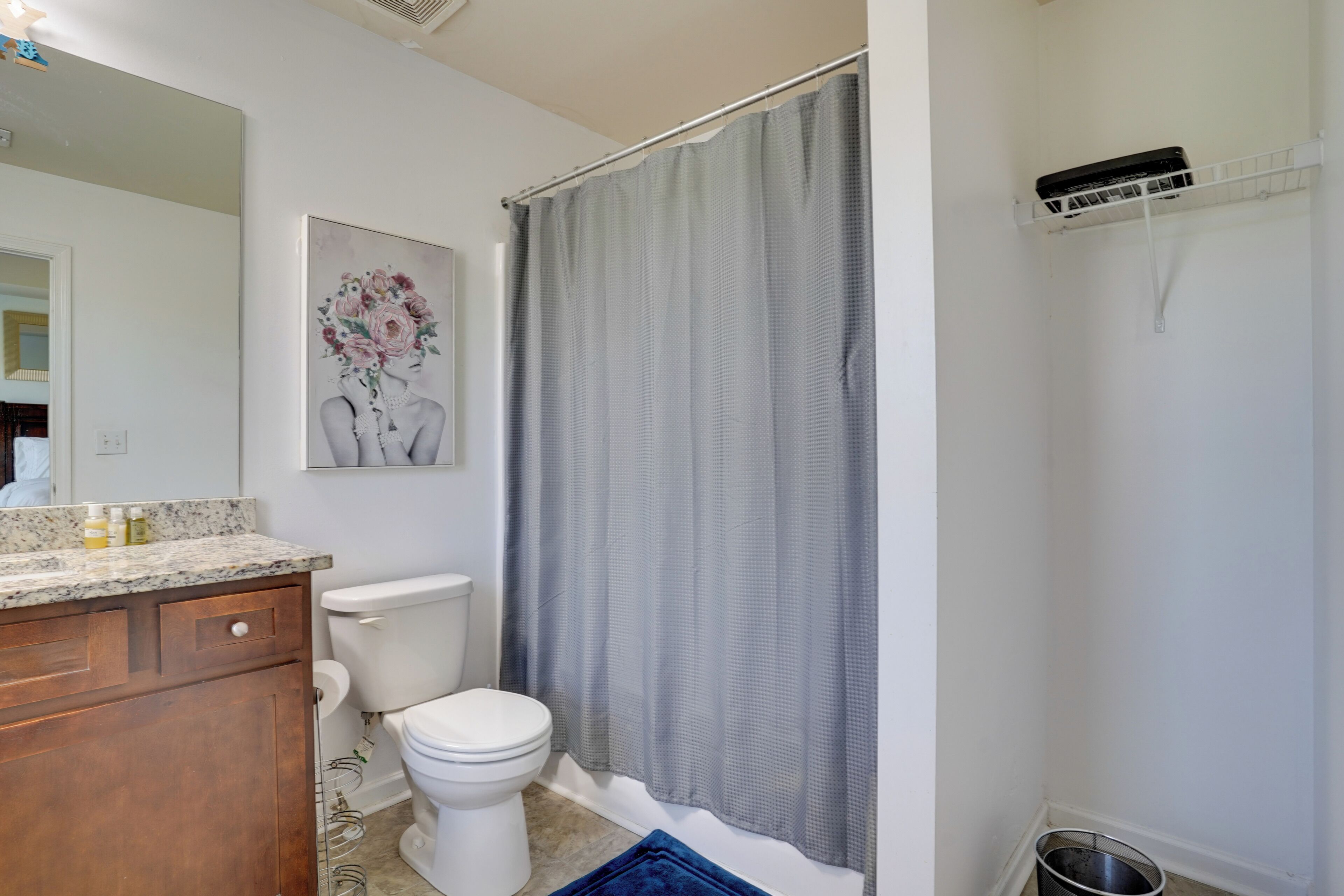 A bathroom with a toilet, a shower curtain, a sink with a marble countertop, and a mirror.