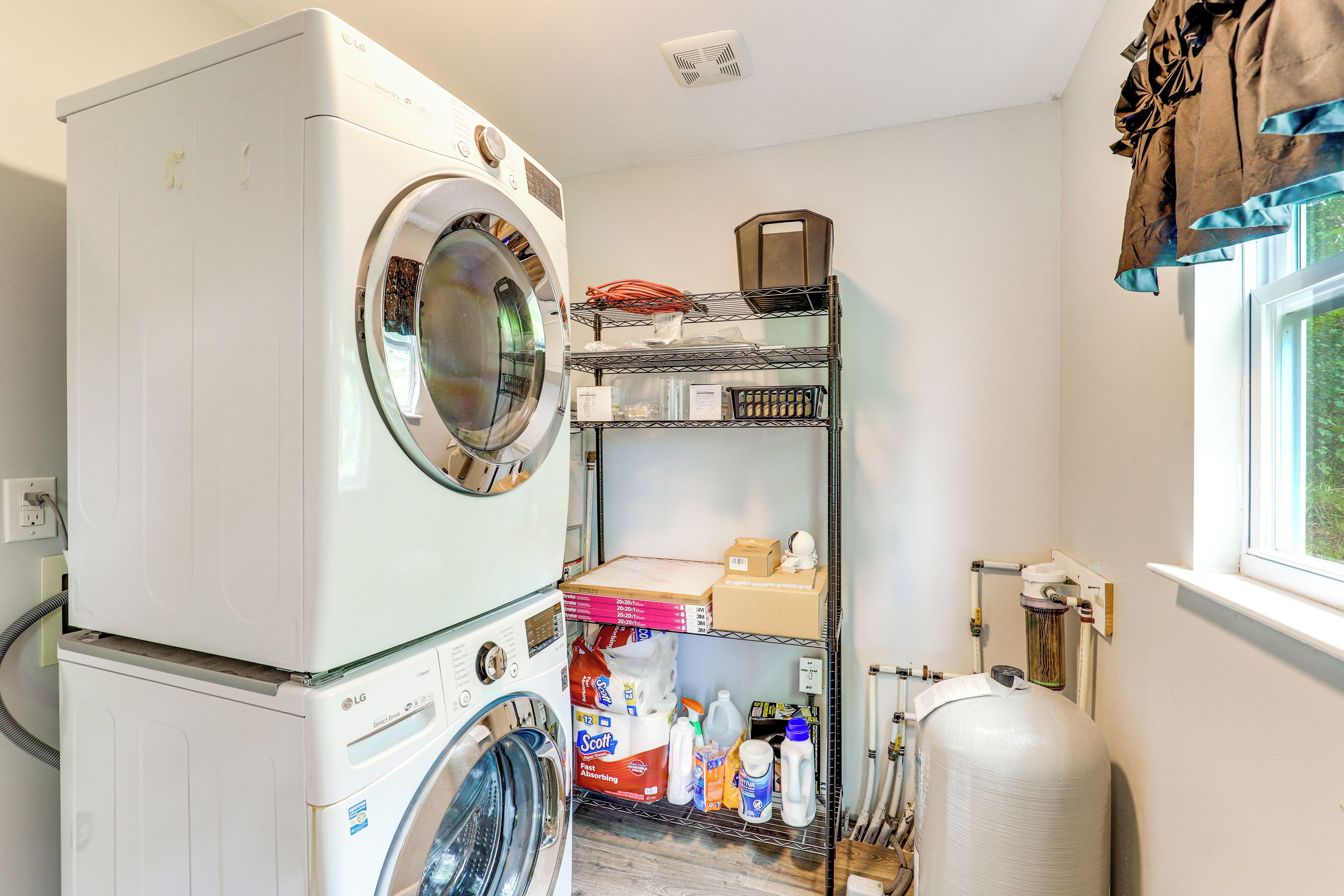 A laundry area with stacked washers and dryers, a metal shelf with supplies, and a large water heater.