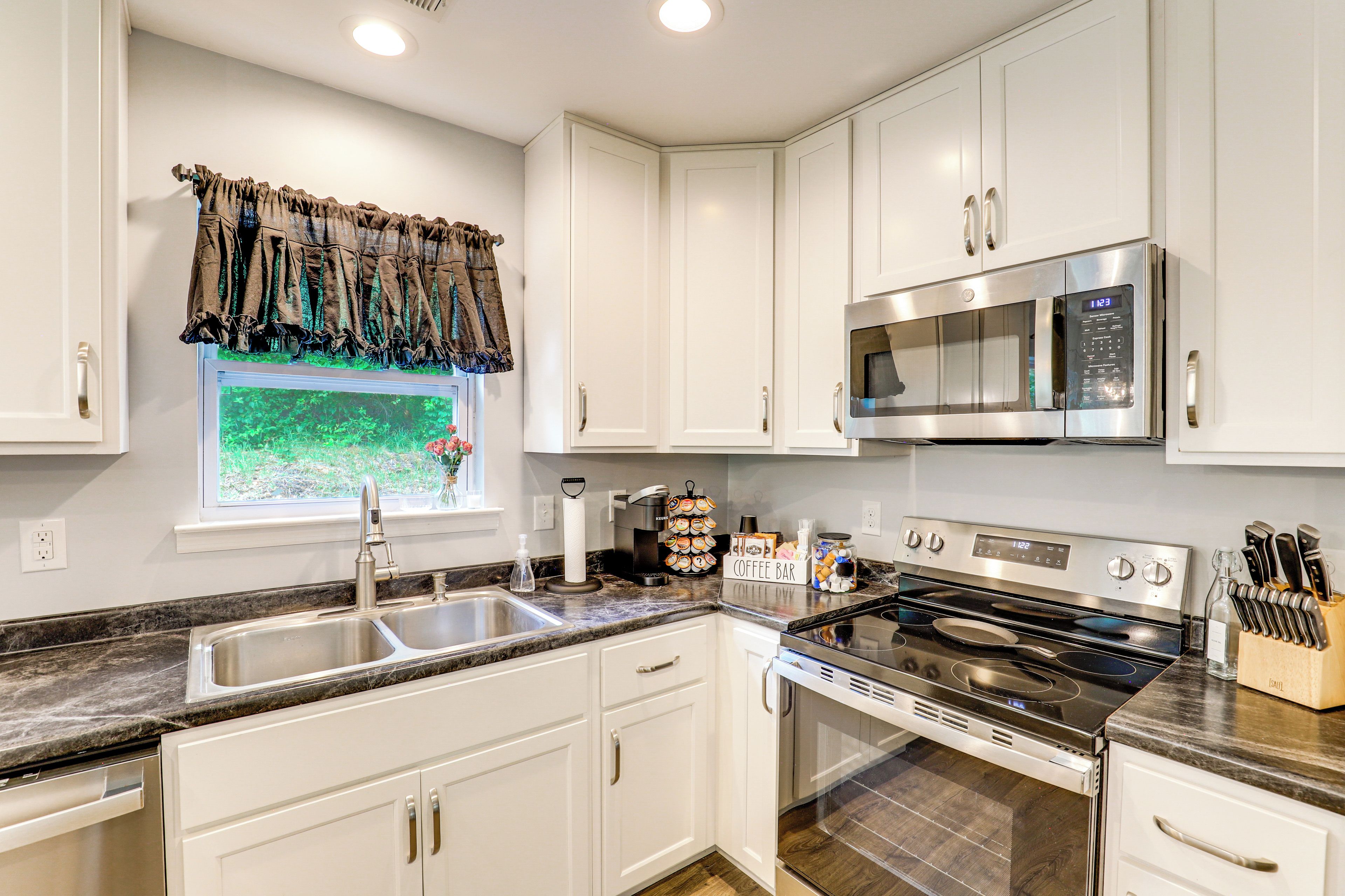 A kitchen with white cabinets, a stainless steel microwave, a stove, and a coffee bar.