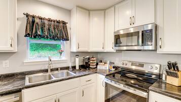 A kitchen with white cabinets, a stainless steel microwave, a stove, and a coffee bar.