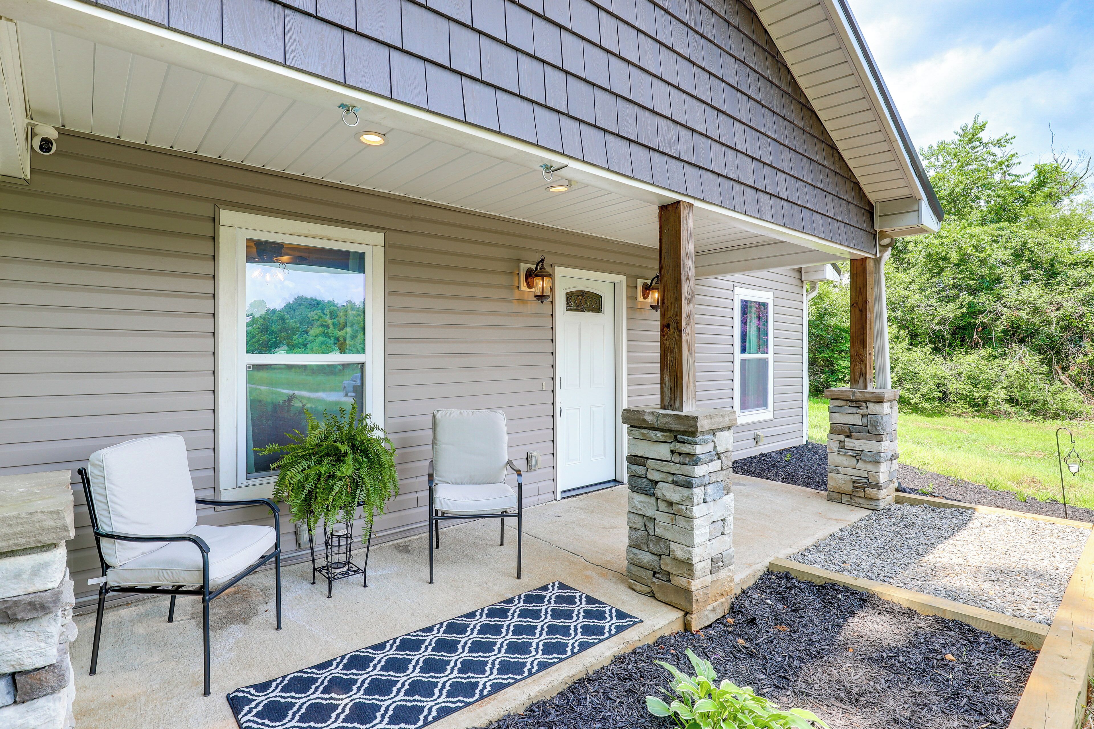 A house with a covered porch, two chairs, a potted plant, and a stone pillar.