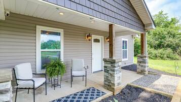 A house with a covered porch, two chairs, a potted plant, and a stone pillar.
