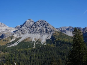 Eine Berglandschaft mit einem markanten Gipfel, bewaldetem Tal und blauem Himmel.