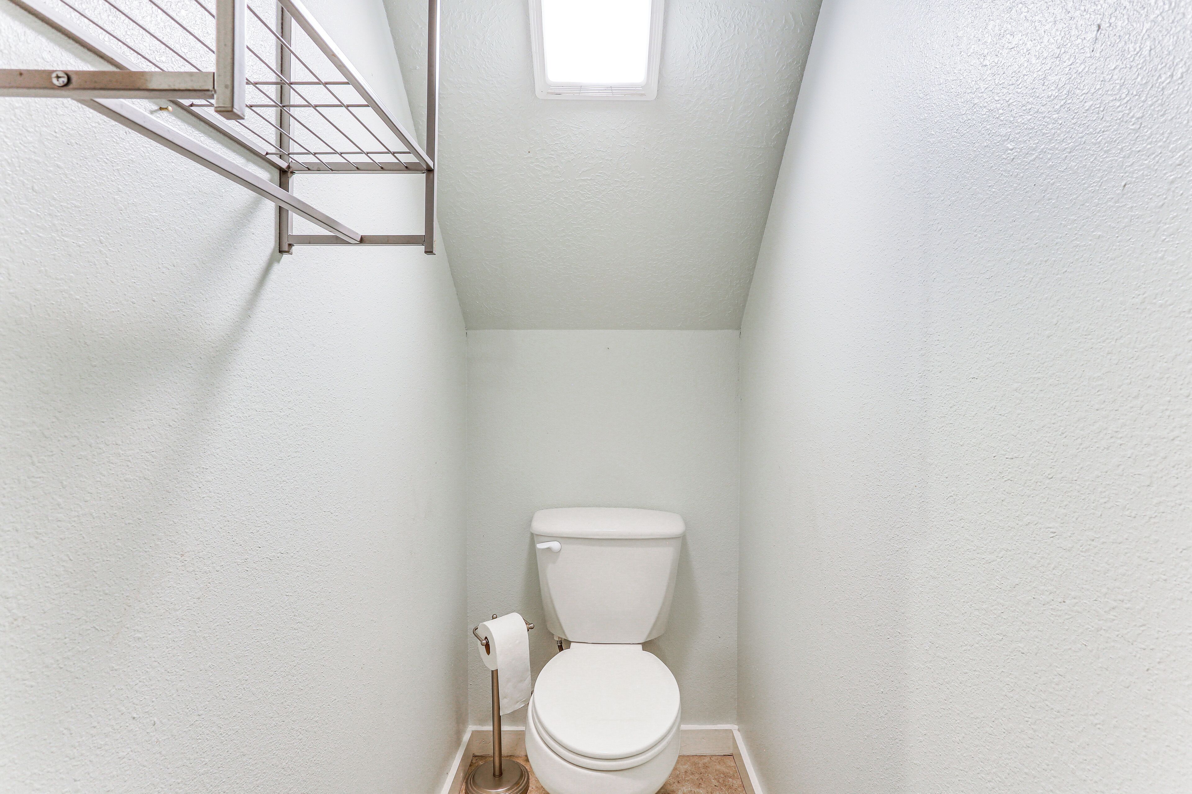 A small, white bathroom with a toilet, a metal rack, and a window.