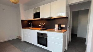 A modern kitchen with white cabinetry, a built-in oven, and a coffee maker on the countertop. - Charming apartment near the beach (Saint-Hilaire-de-Riez)