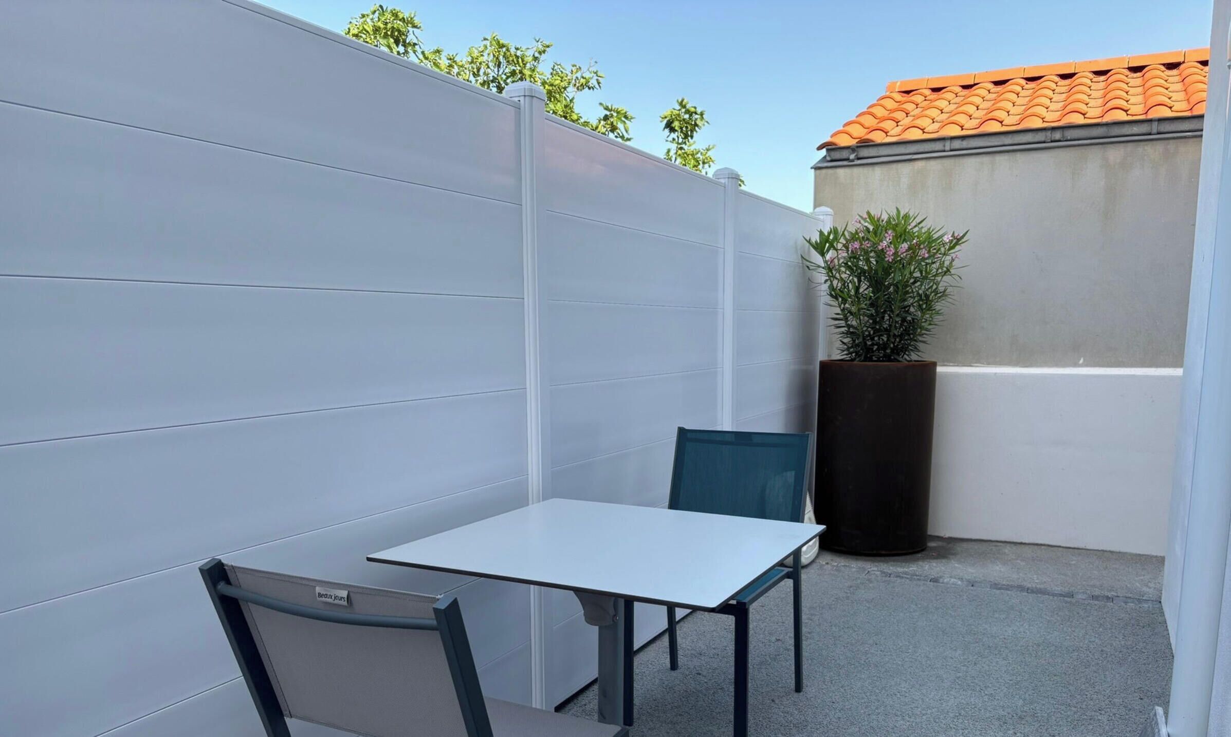 A small outdoor seating area with a table and chairs, a potted plant, and a concrete wall.