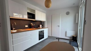 A modern kitchen with white cabinetry, a microwave, and a sink. - Charming apartment near the beach (Saint-Hilaire-de-Riez)