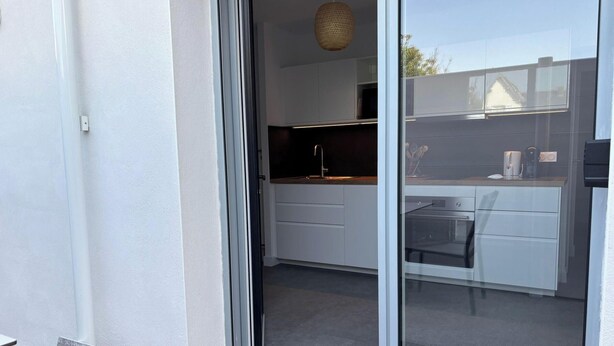 A modern kitchen with white cabinets, a built-in oven, and a hanging light fixture. - Charming apartment near the beach (Saint-Hilaire-de-Riez)