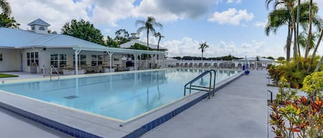 Una piscina con zona relax coperta, palme e cielo sereno.