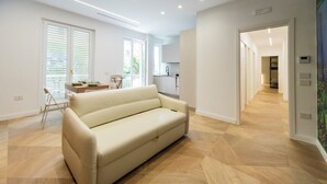 Een moderne woonkamer met een beige bank, een eethoek met een tafel en stoelen, en een keuken op de achtergrond.