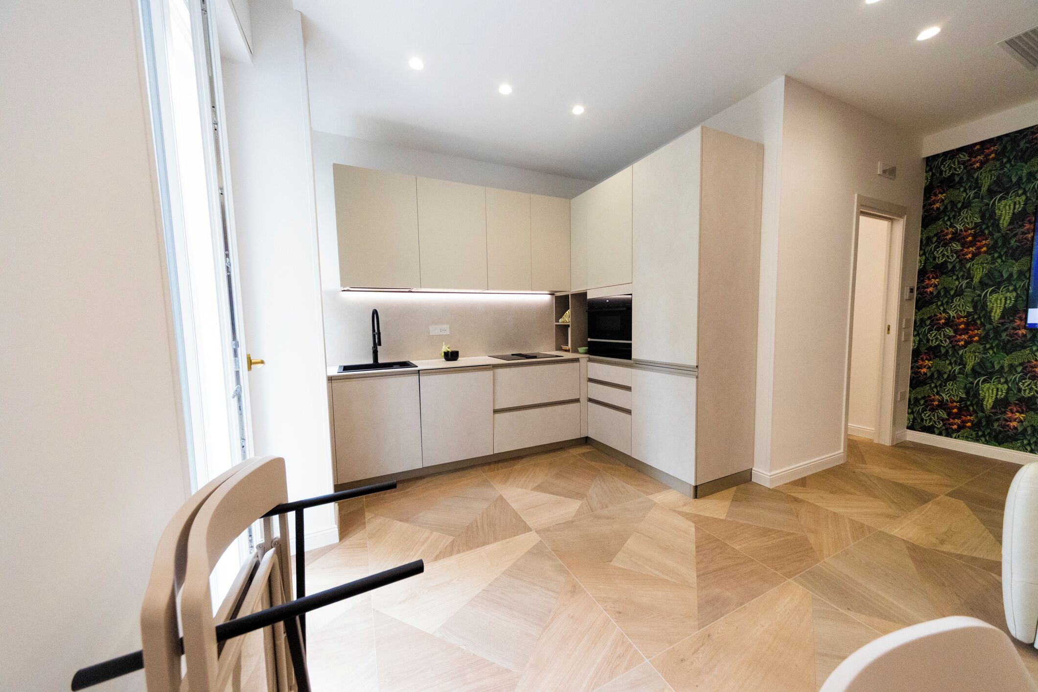 A modern kitchen with white cabinets, a black countertop, and a patterned wall.