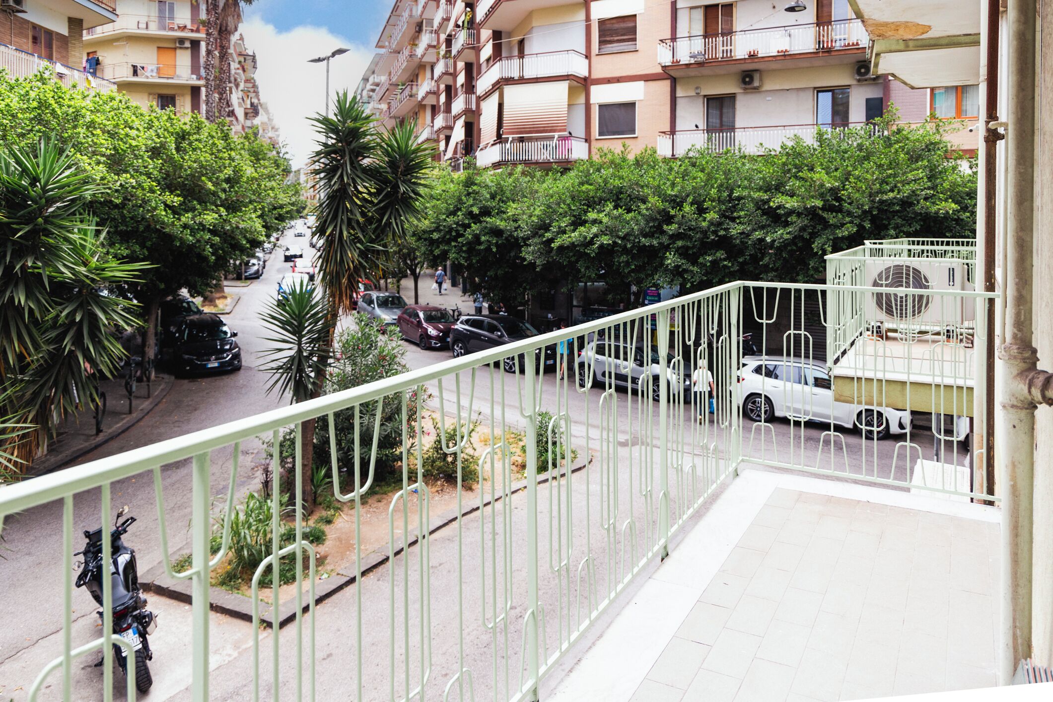 A residential street with parked cars, a motorcycle, and a building with balconies.