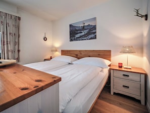 A bedroom with a wooden bed, two bedside tables, a nightstand, a wall-mounted picture, and a curtain with a pattern. - Paradies 411 Appartement/Fewo,  , 2-Bettwohnung 2-Bettwohnung by Interhome (Arosa)