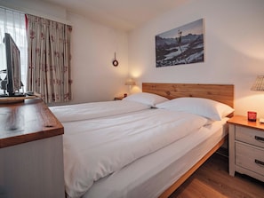 A hotel room with a large bed, a wooden headboard, a nightstand with a lamp, a window with curtains, and a painting on the wall. - Paradies 411 Appartement/Fewo, Bad, WC, 2-Bettwohnung 2-Bettwohnung by Interhome (Arosa)