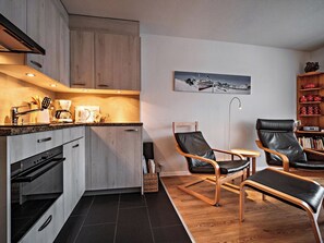 A modern kitchen with dark tiles, wooden cabinets, and a coffee maker. There are two leather chairs and a small table in the living area. - Paradies 411 Appartement/Fewo,  , 2-Bettwohnung 2-Bettwohnung by Interhome (Arosa)