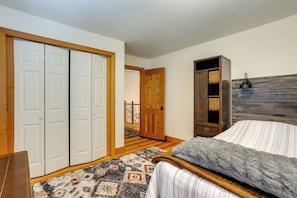 A bedroom with a bed, a wooden wardrobe, a patterned rug, and a door leading to a staircase.