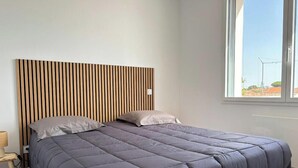 A bedroom with a bed, a headboard, a window, and a nightstand with a lamp. - Apartment near the beach - 6 guests (Saint-Hilaire-de-Riez)