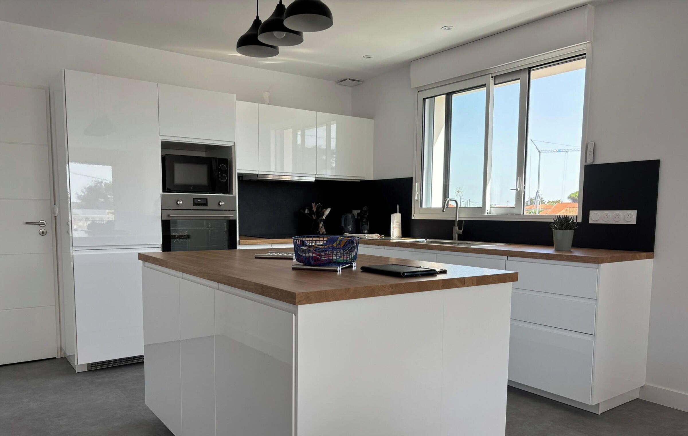 A modern kitchen with white cabinetry, a wooden countertop, and a large window providing natural light.