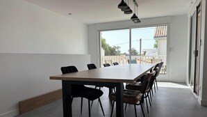A modern dining area with a large table and chairs, a sliding glass door leading to an outdoor patio, and pendant lighting. - Apartment near the beach - 6 guests (Saint-Hilaire-de-Riez)