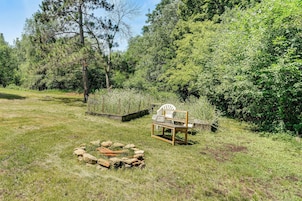 Un espacio al aire libre con césped, una fogata, una estructura de madera y árboles densos al fondo.