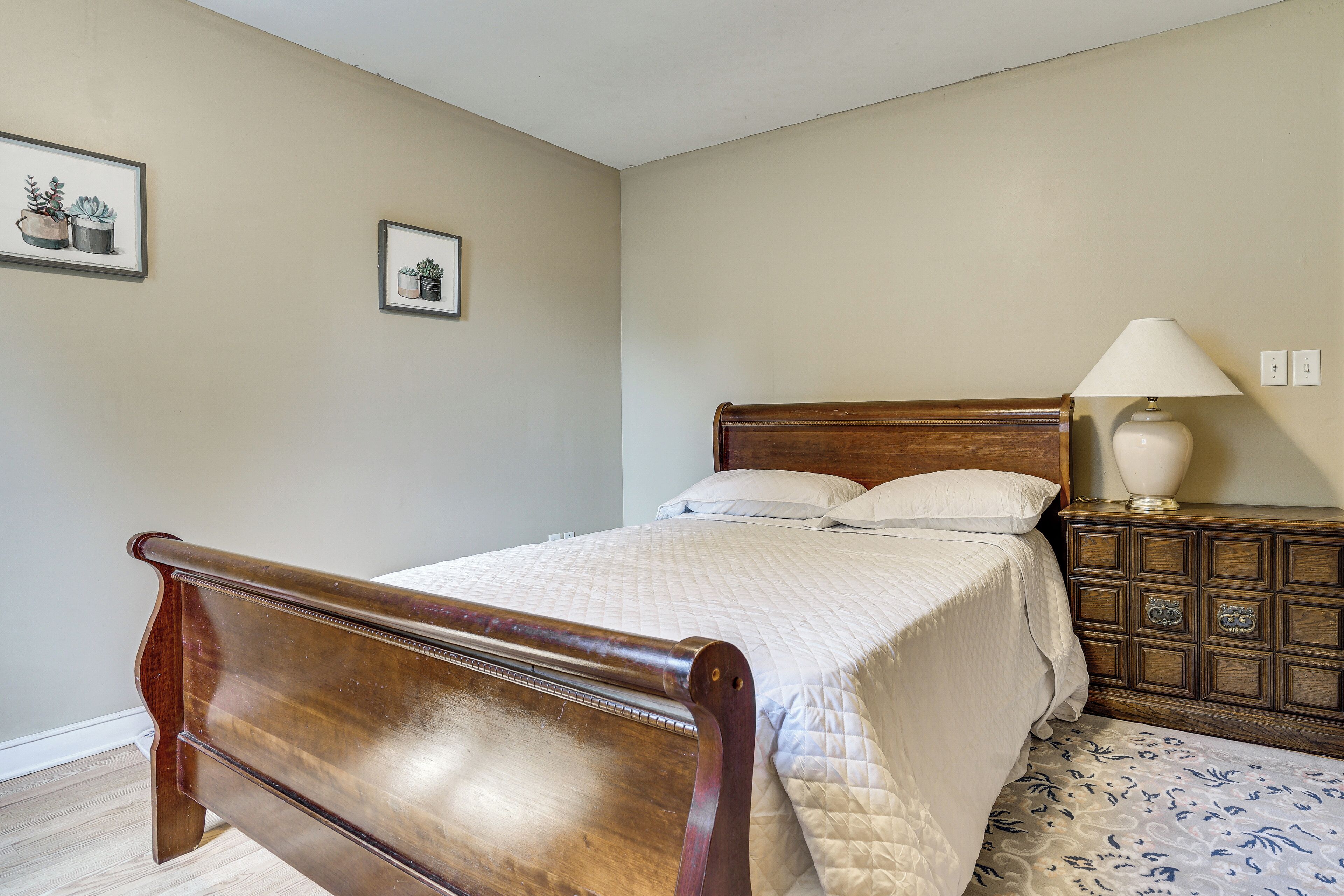 A bedroom with a wooden bed, a nightstand with a lamp, and two framed pictures on the wall.