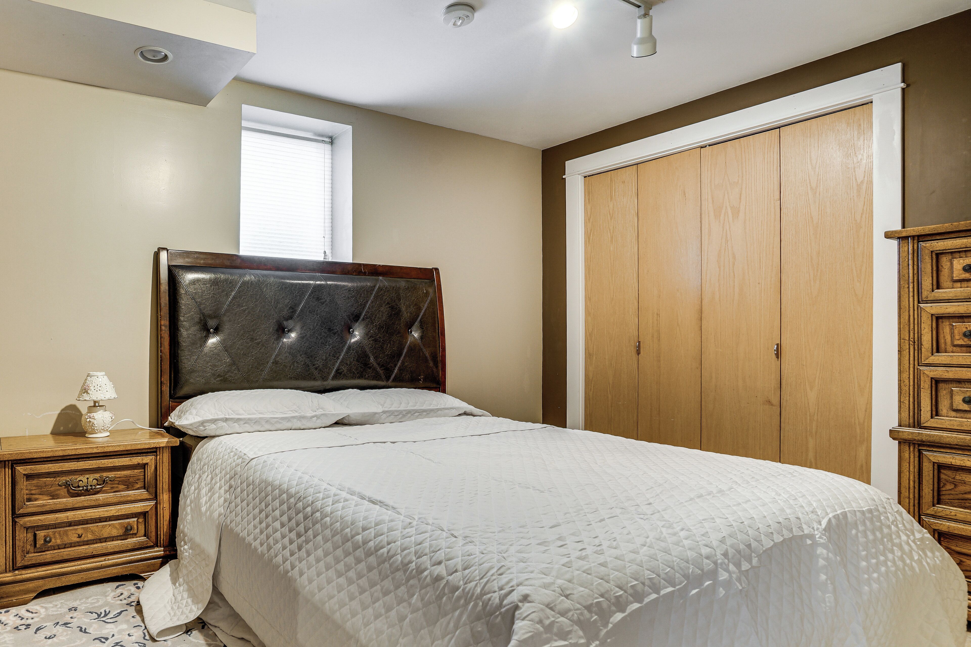 A bedroom with a bed, wooden nightstands, a dresser, a window, and a closet.