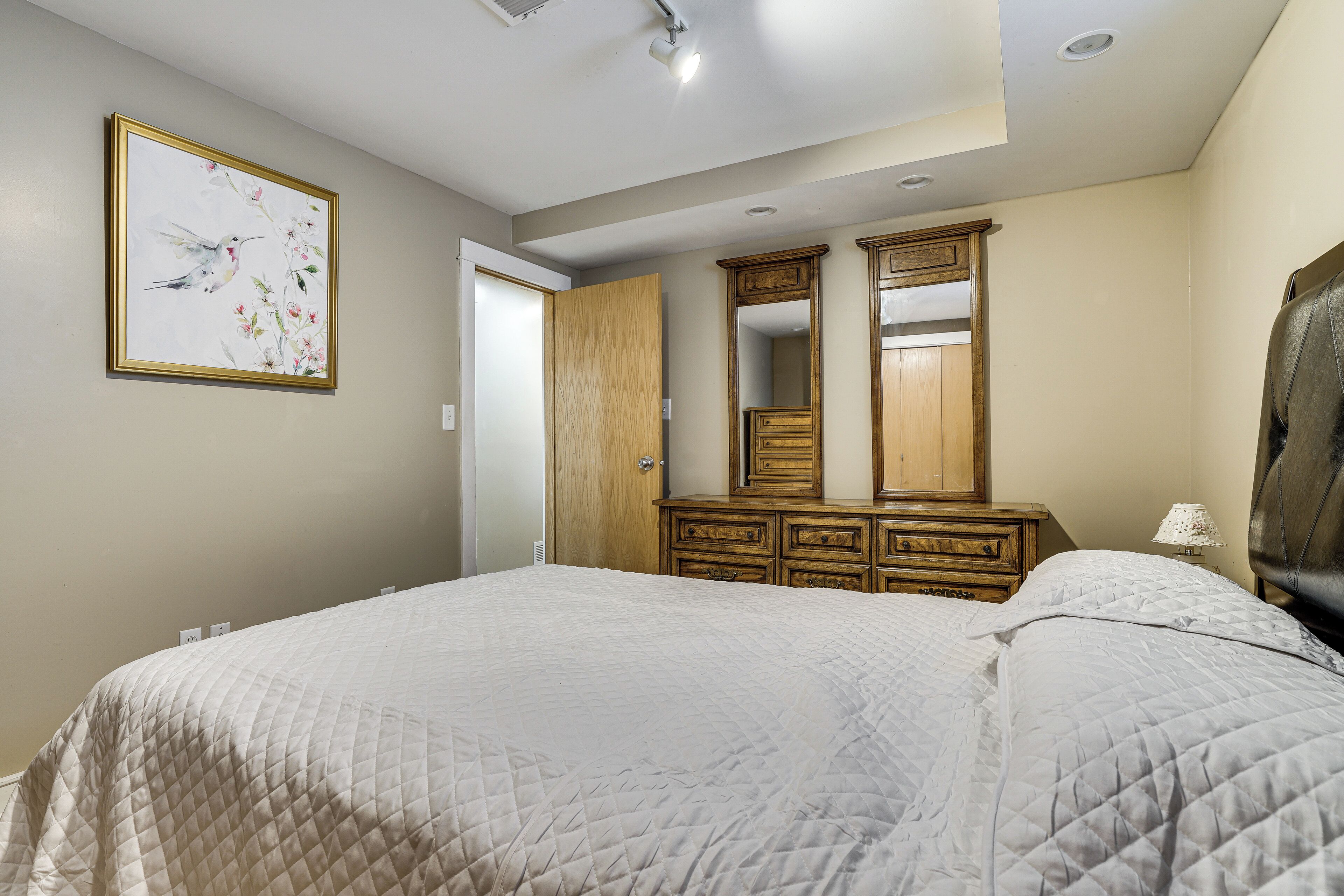 Un dormitorio con una cama grande, un aparador de madera, un espejo y una obra de arte enmarcada en la pared.