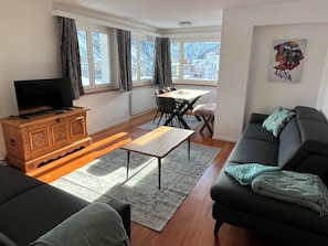 A modern living room with a TV, sofa, dining table, and chairs. - Sunnybank / 2. St. Appartement/Fewo, Dusche und Bad, WC, 9-Bettwohnung by Interhome (Arosa)