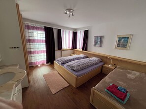 A bedroom with a bed, bedside tables, a nightstand, a window with curtains, a ceiling light, and a wall-mounted picture. - Sunnybank / 2. St. Appartement/Fewo, Dusche und Bad, WC, 9-Bettwohnung by Interhome (Arosa)
