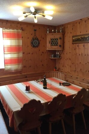 Ein Essbereich mit einem Tisch für vier Personen, Holzwänden, einem Deckenventilator und einem Fenster mit Vorhängen.