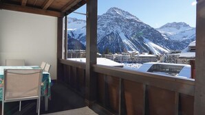 Habitació amb vista a muntanyes cobertes de neu, taula i caires, i sostre de fusta.
