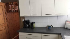 Cuina amb armaris blancs, taule negra i una cafetera.
