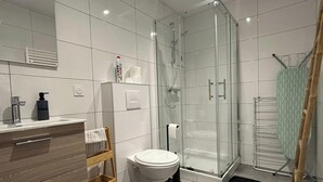 Ein modernes Badezimmer mit Duschkabine aus Glas, Toilette, Waschbecken mit Spiegel und Handtuchhalter.