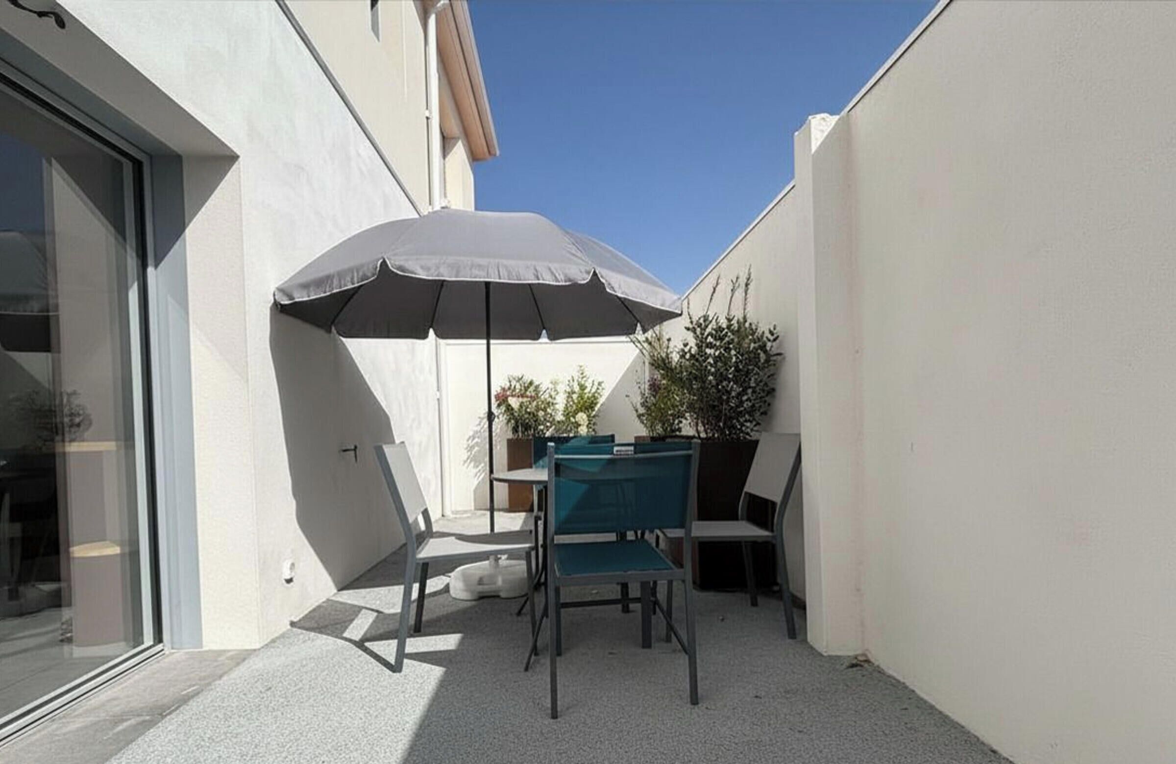 Een terras met een tafel, stoelen, een parasol en een plant in een pot.