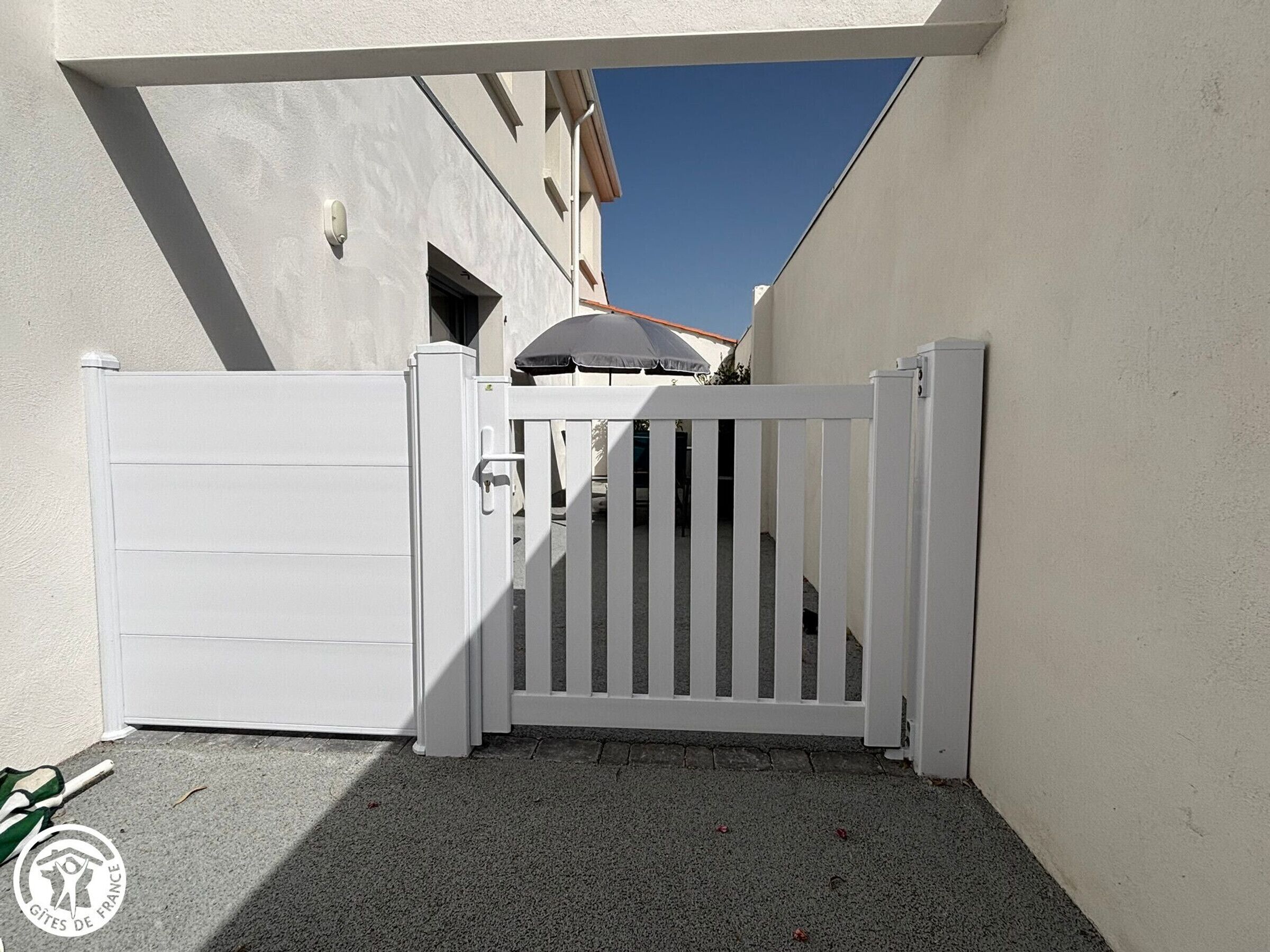 Een poort met een witte poort, een heldere lucht en een gebouw met schuin dak op de achtergrond.